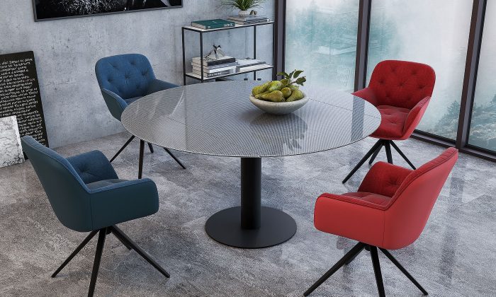 Photo d'ambiance d'une salle à manger avec une table et des chaises. Les piètement sont en acier laqué noir avec un dossier et une assise en tissu/velours en bleu et rouge. Les chaises sont pivotantes.